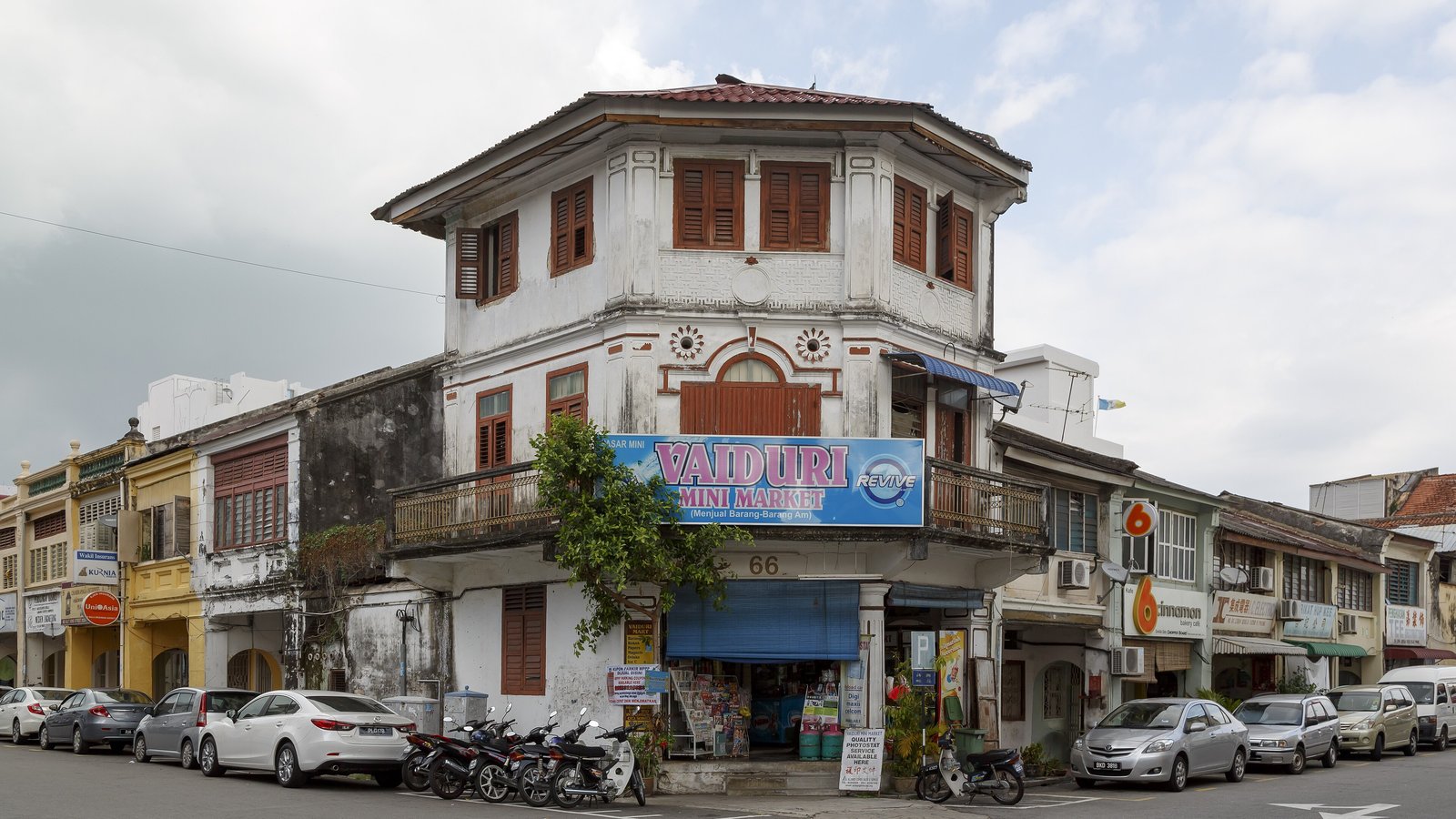 槟城乔治市街角一栋老店屋，楼下是一家迷你市场，门前停着汽车与摩托车